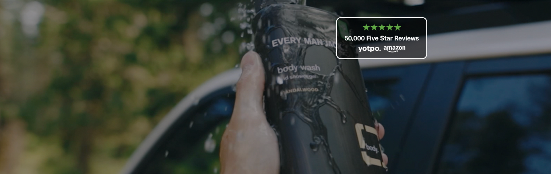 Hand holding Every Man Jack body wash bottle under running water with 50,000 Five Star Reviews badge overlay