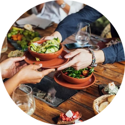 People sharing a meal at a restaurant table with bowls of salad and drinks