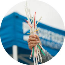 Hand holding a handful of discarded plastic straws in front of a blue Surfrider Foundation event tent